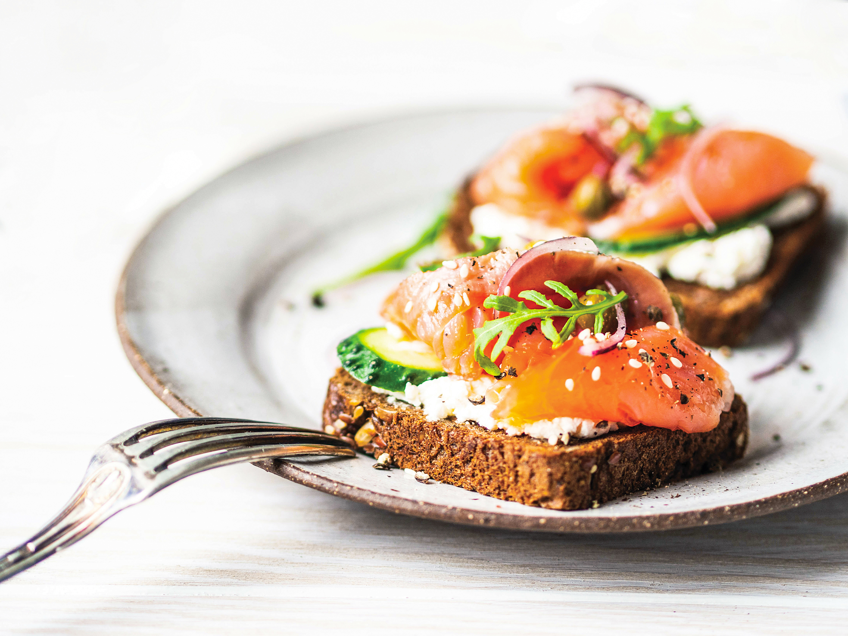 Healthy toasts with rye bread with cream cheese, salmon, fresh cucumber, capers, sesame seeds, black pepper and arugula