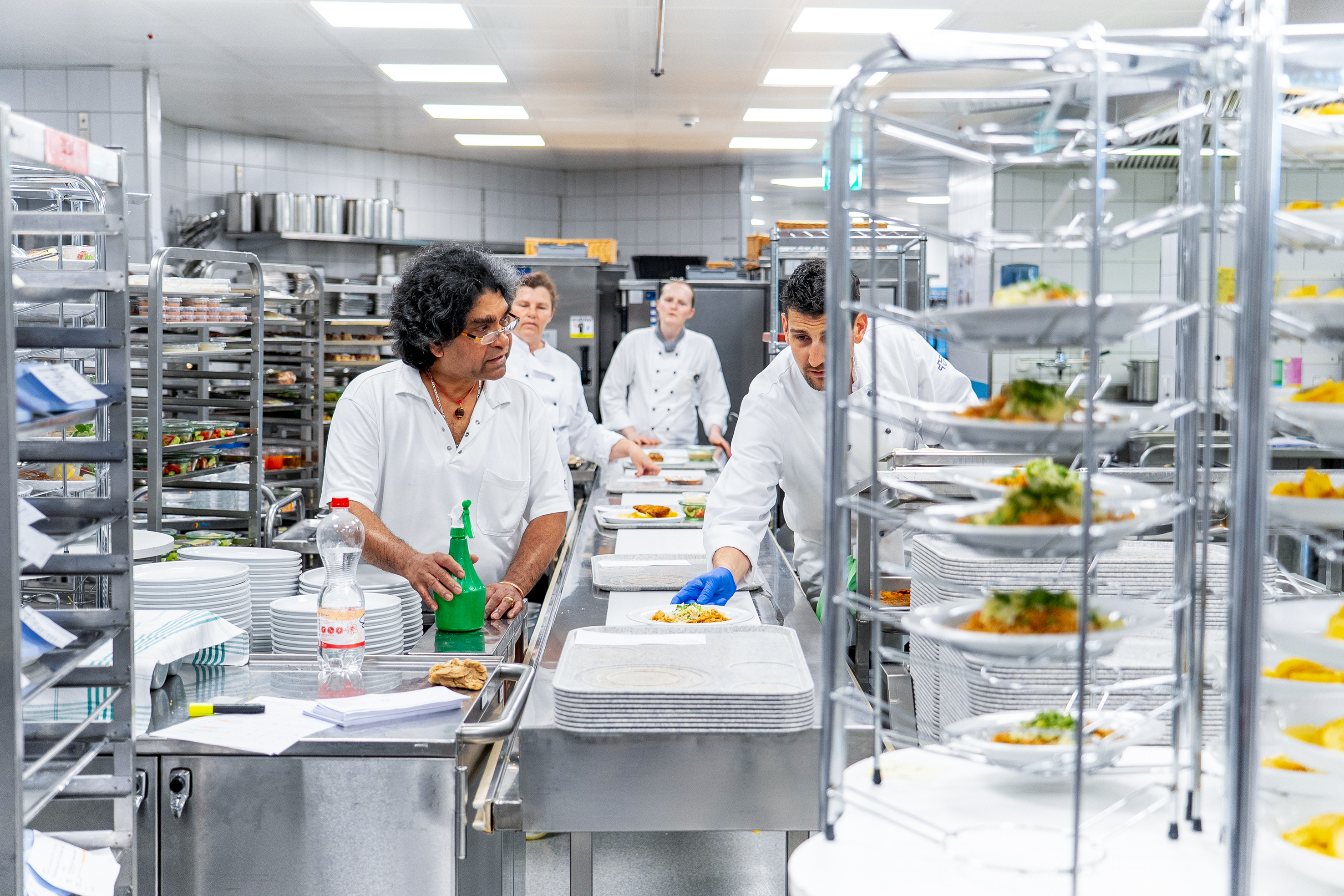 Die angerichteten Kalt- und Warmspeisen werden in den dafür vorgesehenen Geschirrteilen auf dem zentralen Speisenverteilband der Schmalz Distributions-Systeme AG auf dem E-Norm Tablett positioniert.