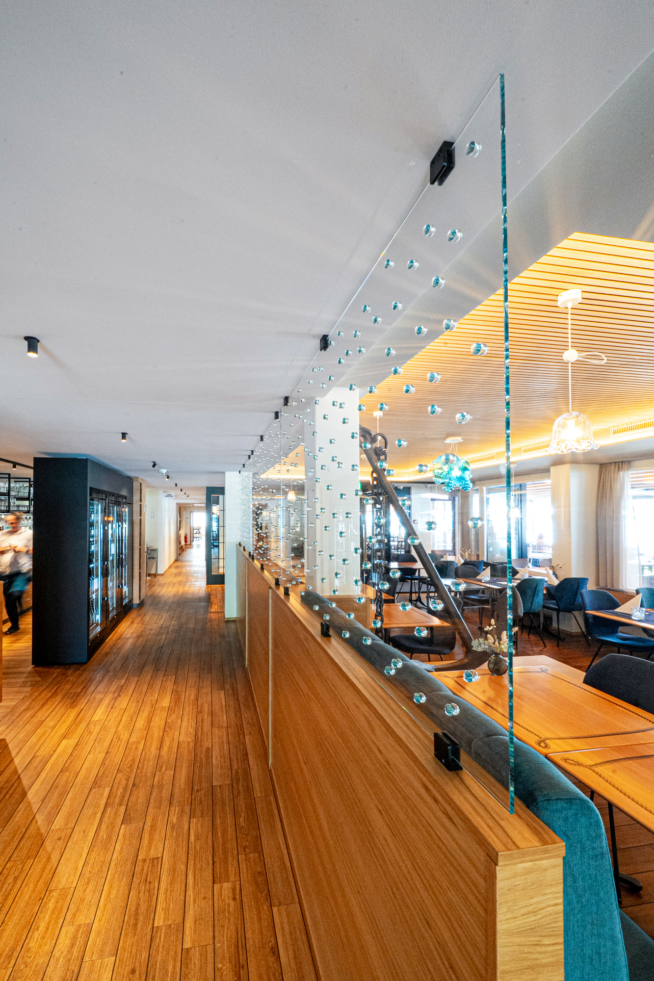 Wo früher Stufen trennten, führt heute eine Rampe von der Gaststube zur Rezeption, begleitet von maritimen Elementen wie Bullaugen, Schiffsseilen und Glasperlen, die Licht und Wasser spiegeln.